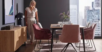 Moderne beere farbene Schalenstühle mit schwarzem Metallfußgestell um einen Esstisch, neben dem eine Frau steht.