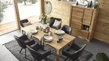 Gemütliches Esszimmer mit einem Esstisch und Highboard aus Massivholz, grauen Schalenstühlen um den Esstisch, der schön gedeckt ist.