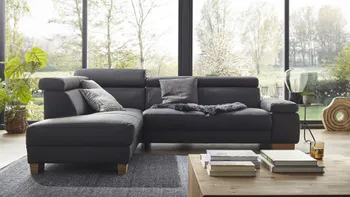 Graues Ecksofa aus Leder mit klappbaren Armlehnen und Kopfstützen dekoriert mit grauen Kissen und einem grauen Fell vor großen Fenstern.