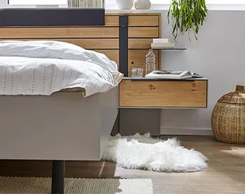 Grauer Nachttisch, der an einem Bett mit Rahmen in grauem Lack befestigt ist und mit Wasserflasche, Glas und Buch dekoriert ist.