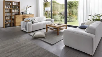 Zwei graue Sofas mit runden Ecken die sich gegenüber stehen und mit Kissen und einer Decke dekoriert sind.