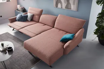 Rosefarbenes Ecksofa mit aufgestellten Kopfstützen und in der Mitte ausgeklappter Fußstütze, dekoriert mit Kissen in blautönen.