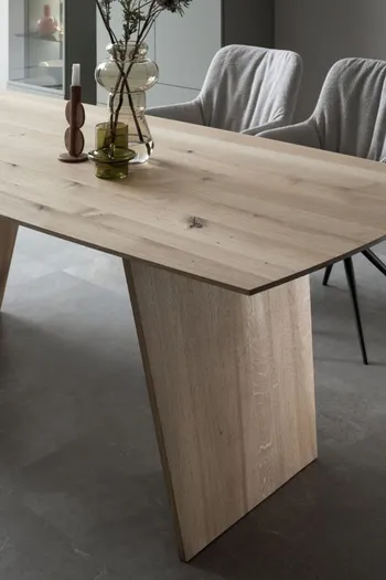 Moderner Massivholz Esstisch mit Fußgestell aus Massivholz, auf dem 2 Vasen und ein Kerzenständer stehen.