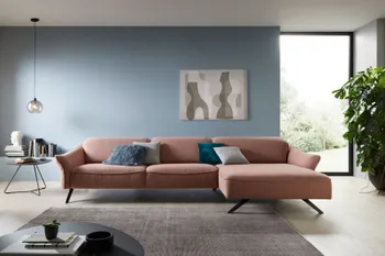 Rosafarbendes Ecksofa mit schwarzen Metallfüßen in einem hellen Wohnzimmer mit schwarzem Beistelltisch.