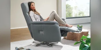 Frau entspannt in graublauem Relaxsessel vor großem Panoramafenster.
