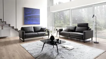 Zwei braune Ledersofas, die im rechten Winkel zueinander stehen, bei dem einen ist eine Kopfstütze hochgeklappt.