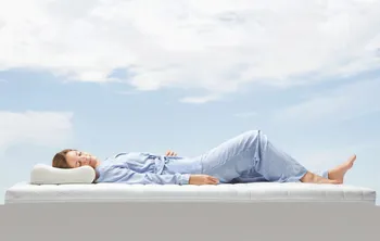 Eine Frau liegt auf einer Matratze unter blauem Himmel.