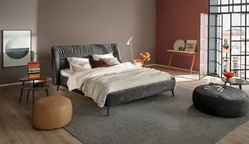 Graues Polsterbett in einem modernen Schlafzimmer, mit beigen, braunem und weißen Kissen und beiger und weißer Decke.
