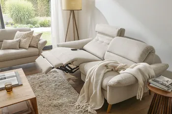 Beiges Sofa in ausgefahrener Relaxposition mit beiger Decke in einem gemütlichem Wohnzimmer.