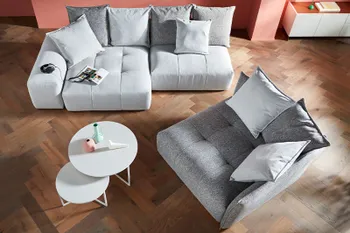 Wohnzimmer in Vogelperspektive mit grauem kleinen zweisitzer und einem grauen Sessel sowie einem runden Couchtisch. 