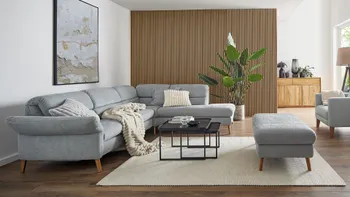 Graues Ecksofa dekoriert mit Kissen und Decke in Grau und Weiß, dazu ein passender Hocker und schwarze Beistelltische in einem modernen Wohnzimmer mit Akkustikpaneelwand.