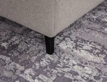 Ecke eines grauen Sofas, das einen schwarzen Metallfuß hat und auf einem gemusterten grauen Teppich steht.