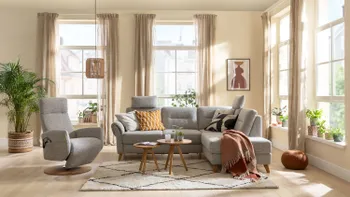 Graues Ecksofa mit bequem gepolsterten Rückenpolster und zwei Kopfstützen neben einem grauen Relaxsessel in einem gemütlichen Wohnzimmer.