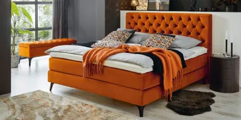 Orangefarbenes Boxspringbett mit passender Strauraumbank in modern eingerichtetem Schlafzimmer. 