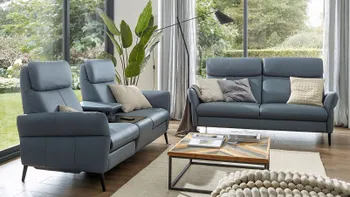 Zwei blaue Sofas mit hoher Rückenlehne, die im rechten Winkel zueinander stehen in einem hellen Wohnzimmer mit einem modernen Couchtisch aus Holz mit Metallgestell.