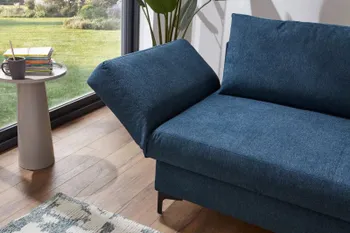 Petrolfarbenes Sofa mit leicht nach oben geklappter Armlehne in einem hellen Raum.