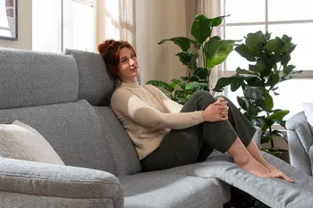 Frau sitzt entspannt auf einem hellgrauen Sofa mit Relaxfunktion.
