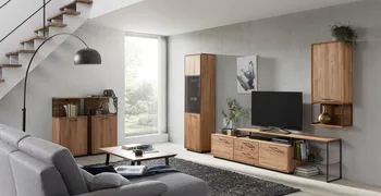 Moderne Wohnwand aus Massivholz mit Griffen und Elementen aus schwarzem Metall in einem gemütlichen Wohnzimmer mit grauem Sofa.