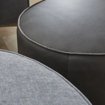 Detailansicht eines schwarzen Lederhockers und eines grauen Hockers.