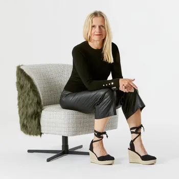 Blonde Frau, die auf einem modernen Sessel sitzt und in die Kamera schaut.
