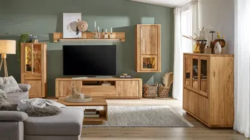 Wohnwand aus Massivholz grifflos bestehend aus TV-Board, Highboard, Wandschrank, Wandregalboden und zusätzlich noch einer passenden Vitrine mit Glasscheiben, dekoriert mit vielen Vasen, Kerzenhaltern und Pflanzen in einem gemütlichen Wohnzimmer.