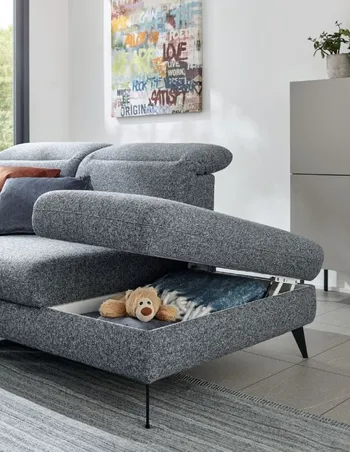 Geöffneter Stauraum unterhalb der Sitzfläche eines grauen Sofas.