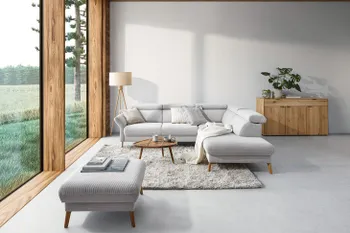 Beiges Ecksofa mit passendem Hocker neben einer großen Fensterwand.