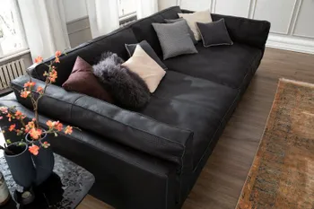 Designer Sofa mit schwarzem Lederbezug und modernen sichtbaren Nähten, hohen Armlehnen und großen Kissen an der Rückenlehne dekoriert mit vielen Kissen in grau, beige und rot.