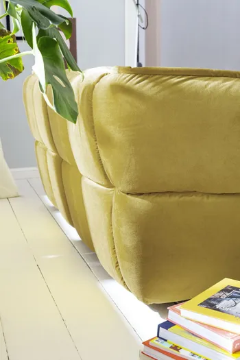 Seitenansicht eines Sofas mit gelbem Stoffbezug und großzügiger Steppung 