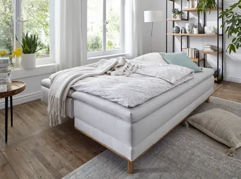 Bild eines weißen Sofas, das umgebaut ist zum Bett und mit weißen Decken und Kissen und grünem Kissen dekoriert ist.