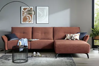 Rotes Ecksofa mit Quernähte an den großen Rückenkissen und schwarzen Metallfüßen in einem hellen Raum.