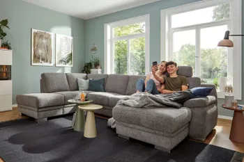 Graue Wohnlandschaft mit silbernen Füßen, auf dem ein Junge und ein Mädchen nebeneinander entspannt auf dem Longchair sitzen.