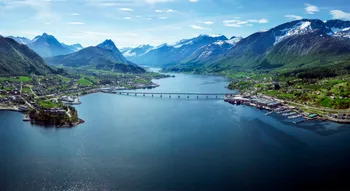 Atemberaubende Luftaufnahme von Sykkylven, Norwegen – die Heimat der Marke Svane®. Die beeindruckende Landschaft mit fjordähnlichen Gewässern, einer Brücke und schneebedeckten Bergen verkörpert die natürliche Schönheit und Ruhe der Region.