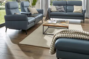 Blaues Ledersofa mit erhöhter Rückenlehne neben einem weiteren blauen Sofa mit hoher Rückenlehne mit dazu passendem Hocker.
