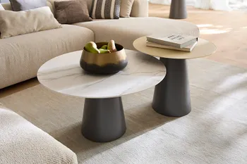 Zwei runde Couchtische vor einem beigen Ecksofa, mit schwarzem Fuß und weißer oder gelber Tischplatte.