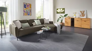 Helles Wohnzimmer mit Ecksofa aus grünem Stoff und einer Kommode.