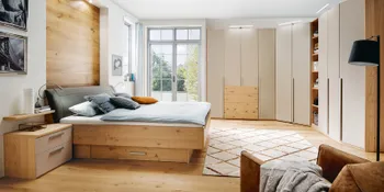 Helles Schlafzimmer mit Bett und Kleiderschrank mit Holzelementen und weißen Schrankfronten.