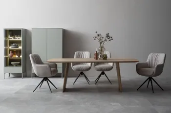 Moderner großer Esstisch aus hellem Holz in einem hellen Raum, um den vier graue Armlehnstühle mit schwarzem Gestell stehen.