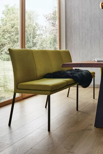 Grüne Esszimmerbank mit schwarzen Füßen an einem Esstisch aus Holz.