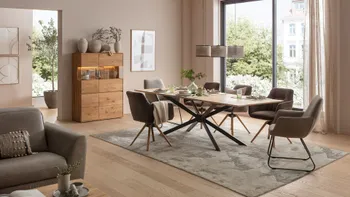 Großer Esstisch aus Massivholz mit Armlehnstühlen in grau in einem hellen Esszimmer mit Blick ins Grüne.