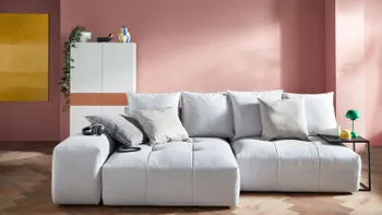 Hellgraues bodentiefes Sofa mit gemütlichen Kissen am Rücken. 