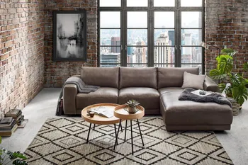 Ecksofa in Leder braun mit großen bequem gepolsterten Rückenpolstern dekoriert mit schwarzen Decken in einem hellen Wohnzimmer im Industrial Look.