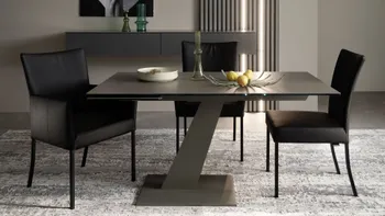 Kleiner Design Esstisch mit schwarzer Tischplatte und grauem schrägem Tischgestell, um den Tisch stehen drei schwarze Stühle.