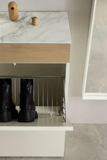 Weißer Designer Schuhschrank mit Klapptüren, bei dem eine geöffnet ist und Blick auf ein schwarzes Paar Schuhe freigibt, die Abdeckung des Schrankes ist eine weiße Keramikplatte in marmor Optik.
