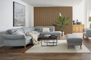 Großes graues Ecksofa mit ausklappbaren Kopfstützen mit passendem Hocker und einem Couchtisch aus schwarzem Metall.