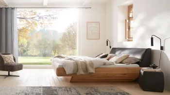 Helles Schlafzimmer mit Doppelbett aus Massivholz und mit gepolstertem Lederkopfteil, passenden Nachttischen und Loungesessel.