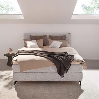 Graues Design Boxspringbett zwischen zwei Dachfenstern.