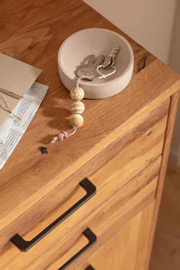 Garderobe aus Massivholz mit schwarzem Griff, auf der eine graue Schale mit einem Schlüssel liegt.