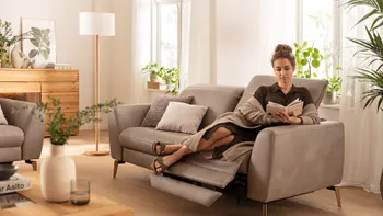 Graues Relaxsofa mit ausgefahrenem Fußteil, auf dem eine Frau entspannt sitzt und ein Buch liest.
