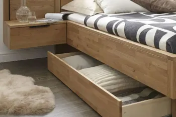 Bett aus Massivholz mit am Bett befestigter Nachtkonsole und einer geöffneten Stauraum Schublade unterm Bett.